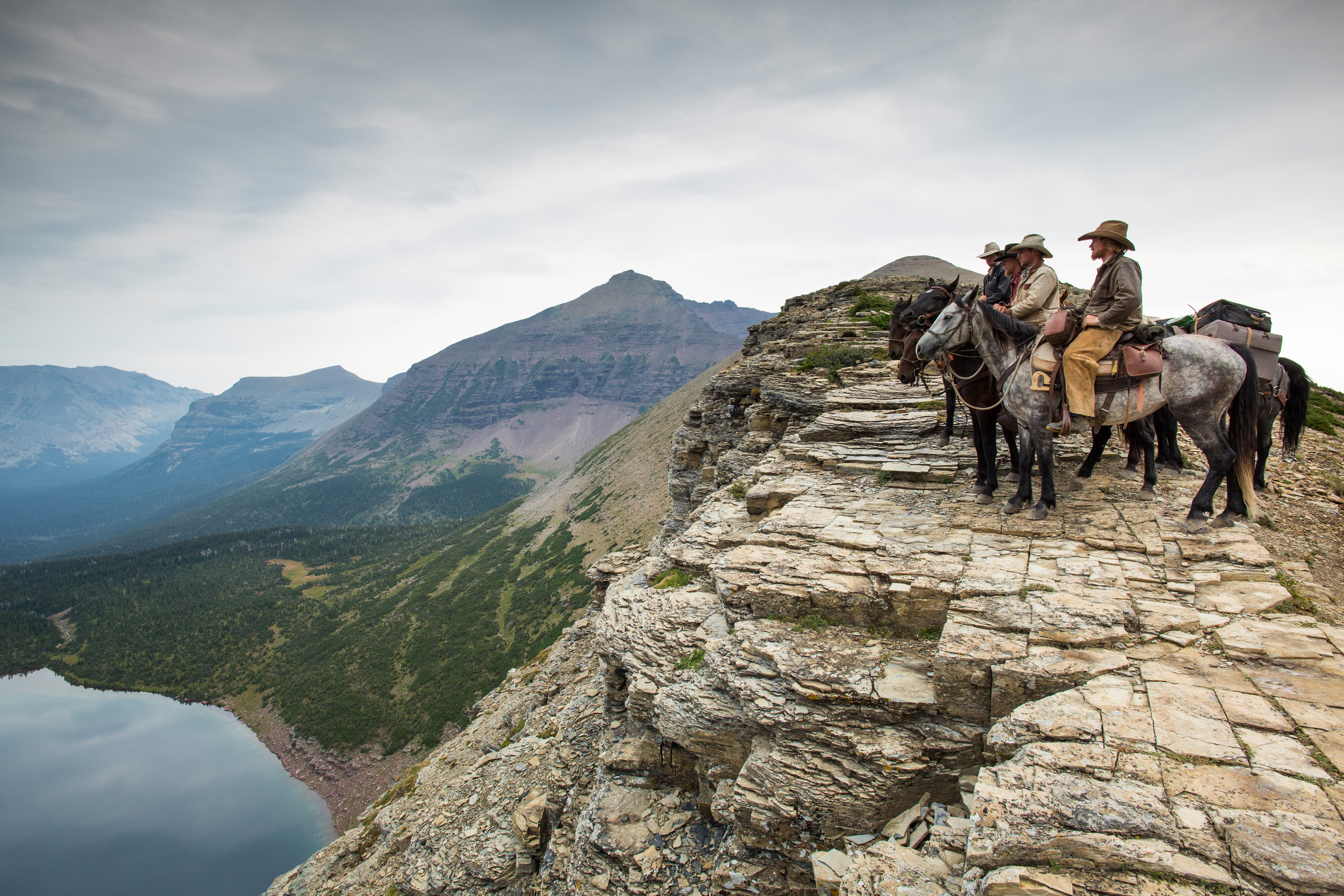 Vier Cowboys auf ihren Pferden am Abgrund eines Steilhangs blicken in die Weite.