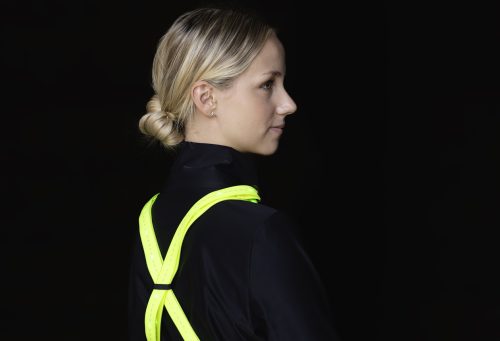 Frau in schwarzem Pulli vor schwarzem Hintergrund mit leuchtender Weste.